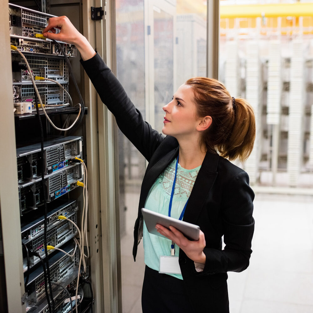 Technician holding digital tablet while examining server in server room
